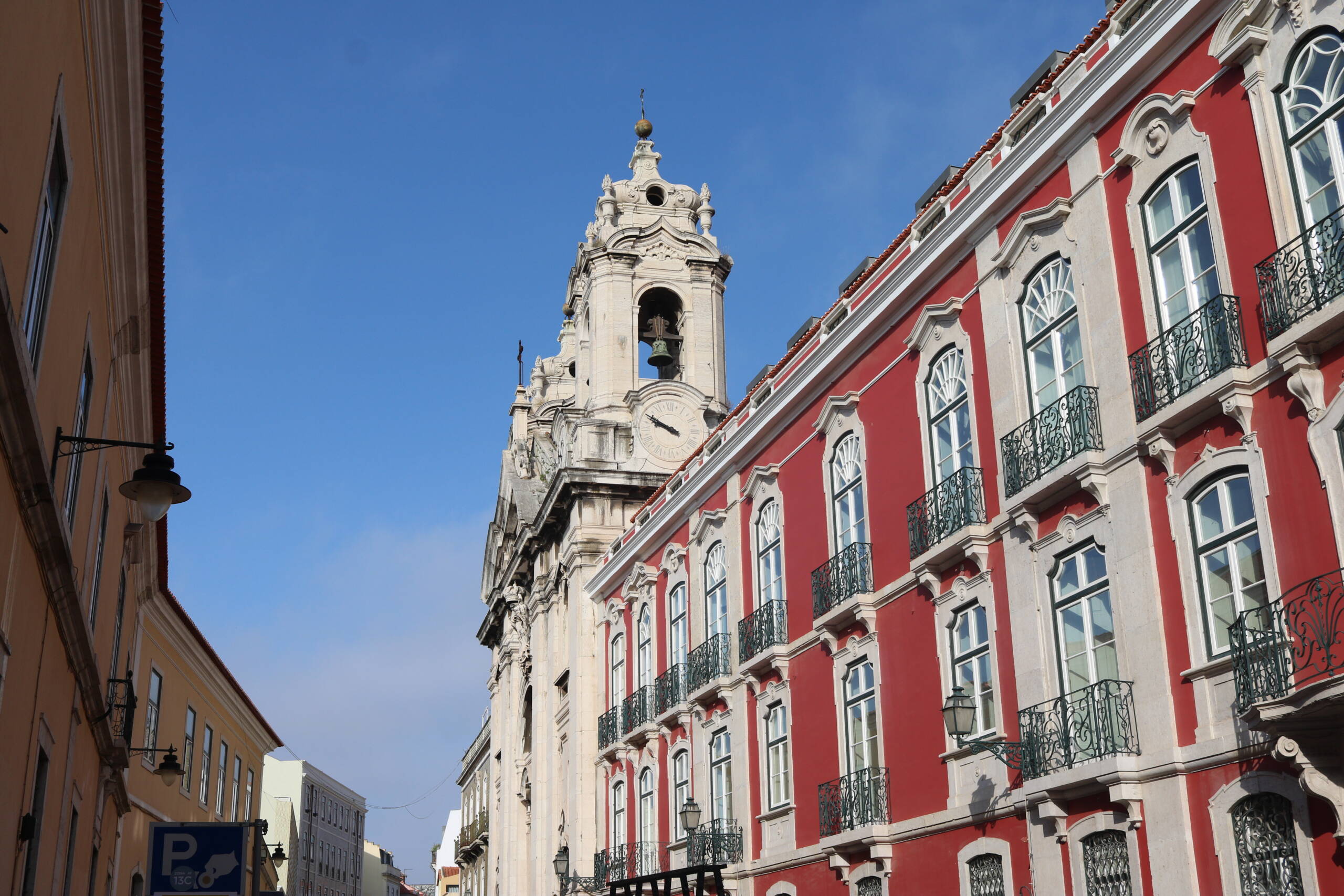 A deep red Pombaline building alongside a white Baroque church tower in Lisbon's Chiado district