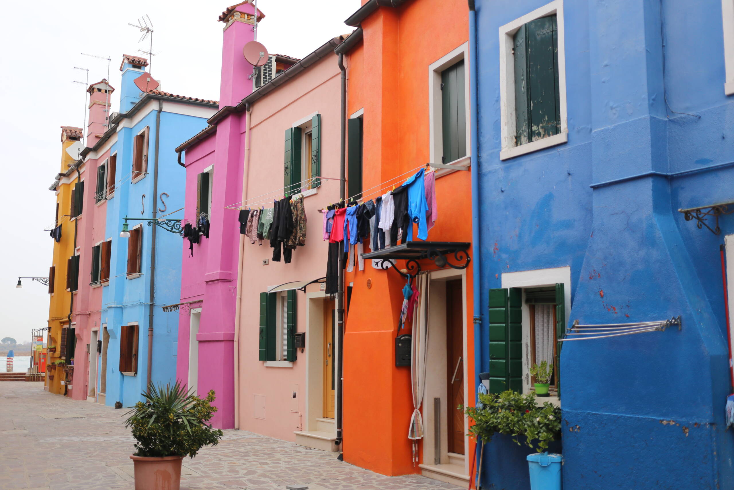 Empty back street on Burano with laundry hanging between pink orange and blue painted houses
