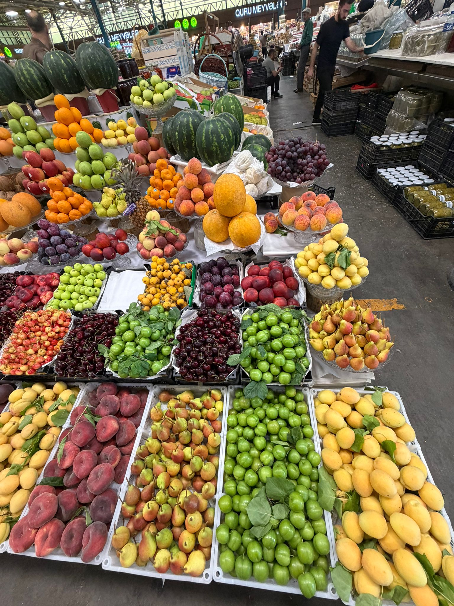 Pyramids of seasonal fruit — apricots, peaches, cherries, green sour plums, melons and watermelons — at a stall in Teze Bazar, Baku The summer table at Teze Bazar — apricots, donut peaches, cherries, and crates of green alça, the sour plum eaten unripe.