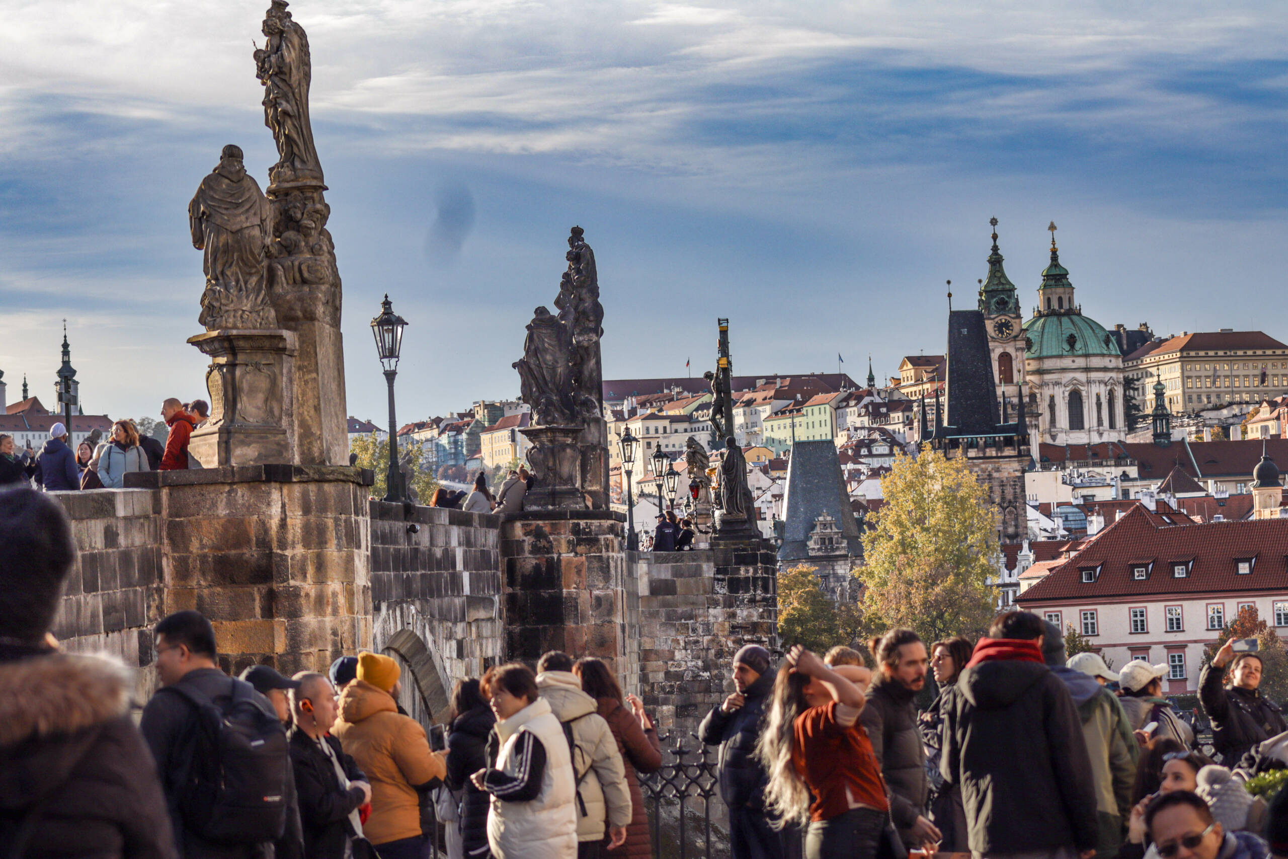 Crowds on Charles Bridge in Prague on an autumn morning, baroque statues on the parapet and the domes and towers of Malá Strana behind