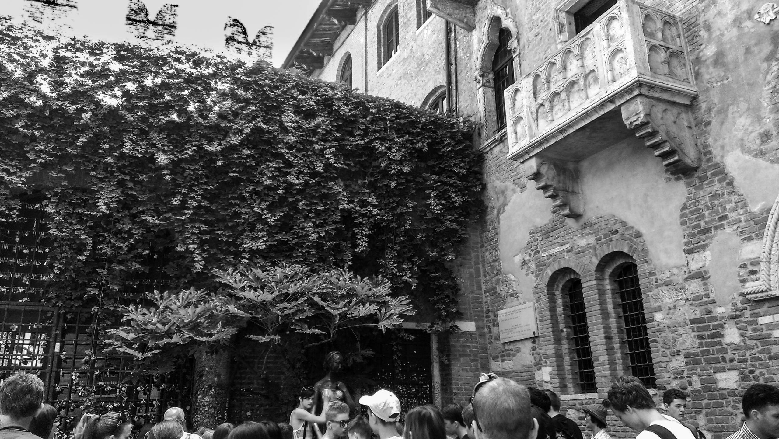 Crowds in the courtyard of Casa di Giulietta in Verona, with the stone balcony and ivy-covered wall above