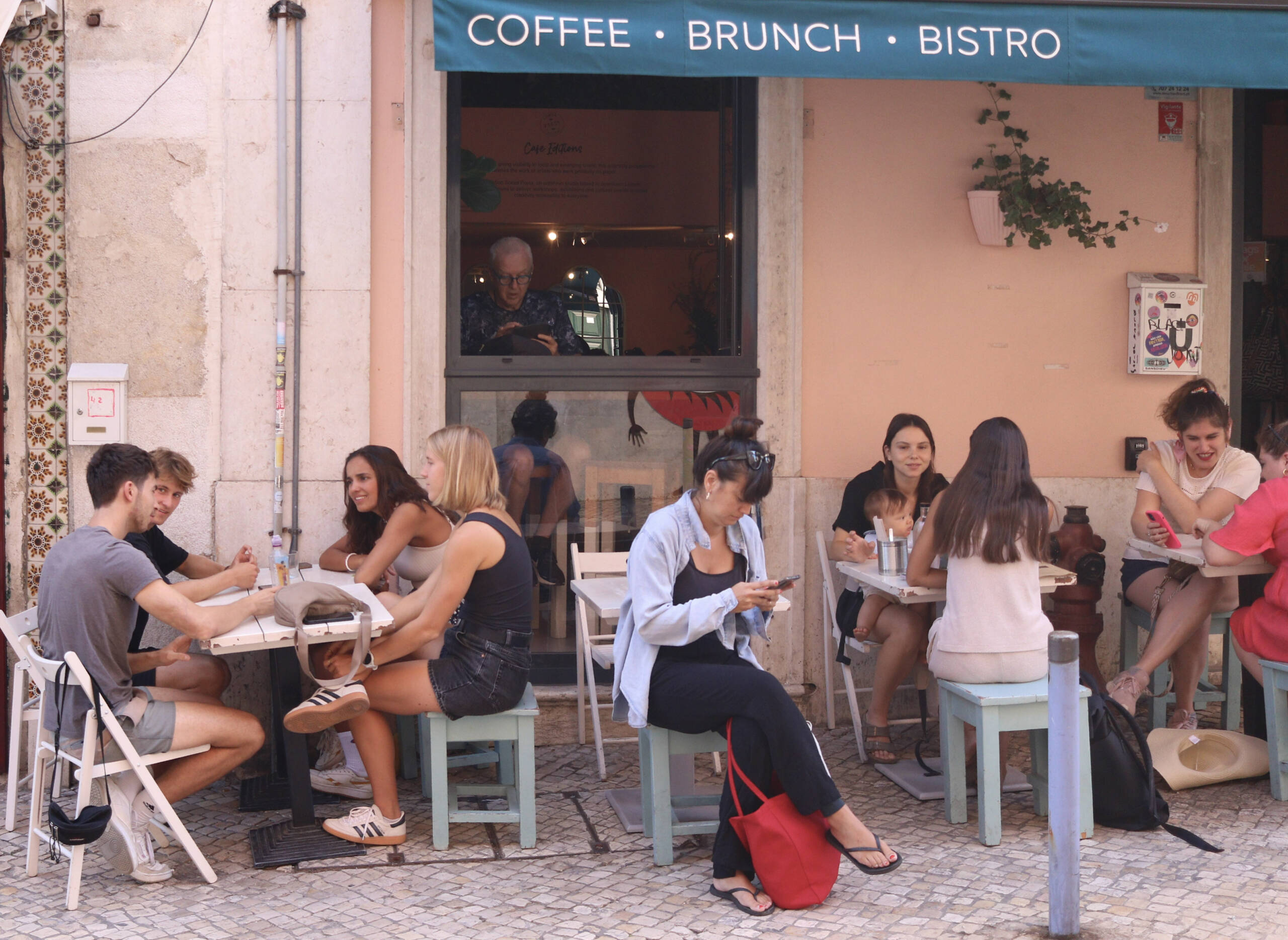 Customers at outdoor tables of a Lisbon coffee and brunch café with a teal awning