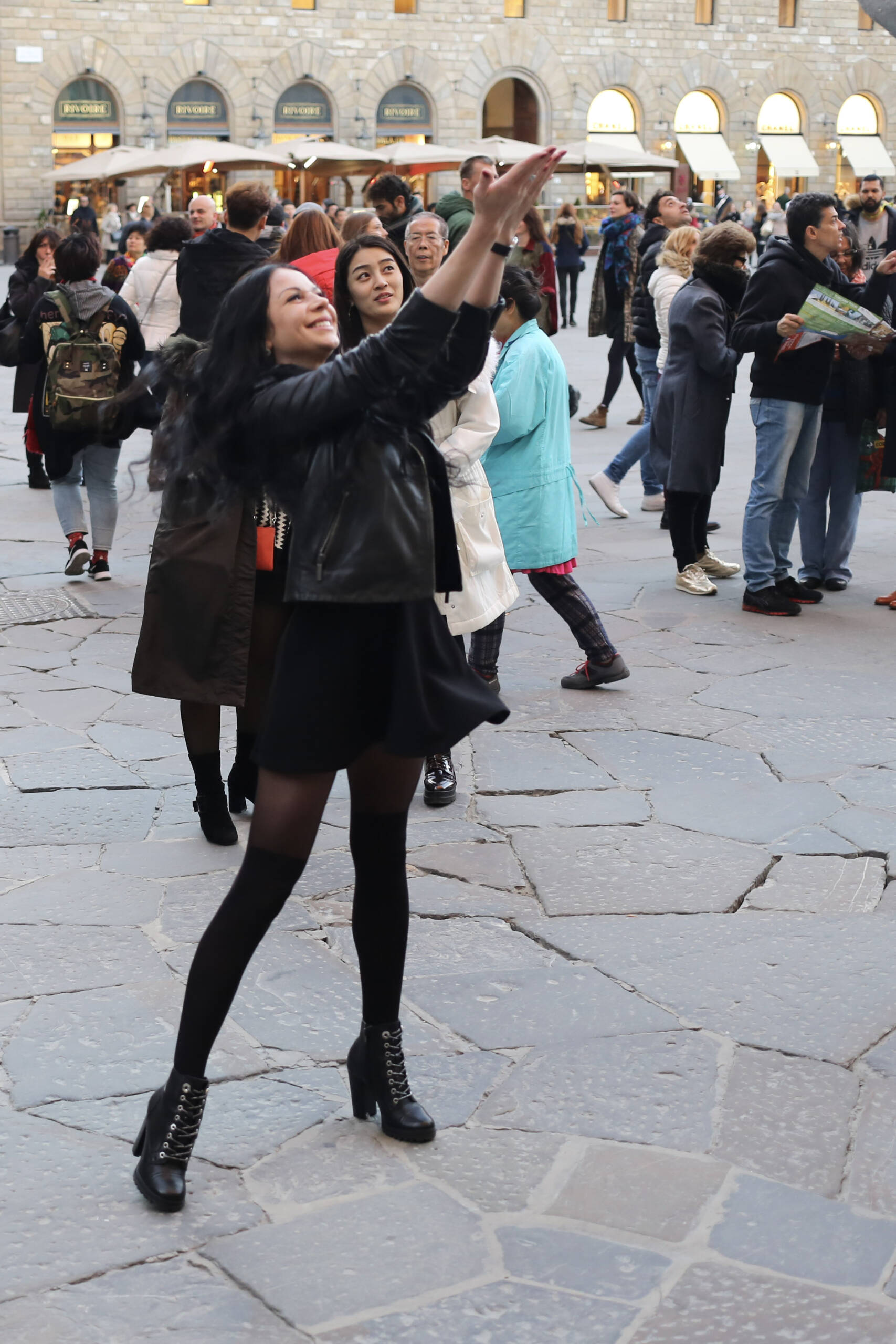 A woman tourist stands in Piazza della Signoria with her arm raised, pretending to hold the David's testicles for an Instagram photo