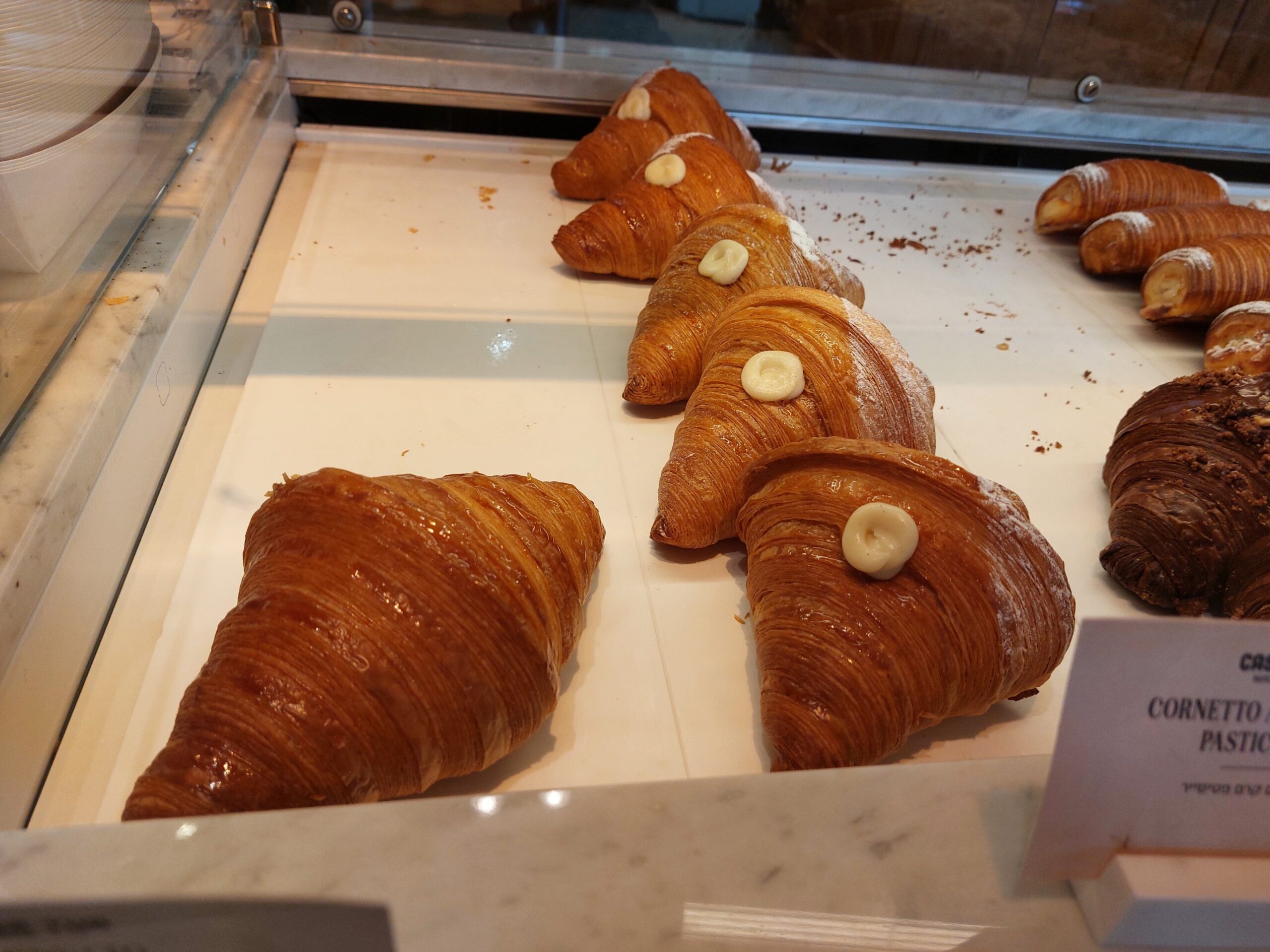A row of glossy laminated cornetti at Casa Tua, most with a dot of pistachio cream on top