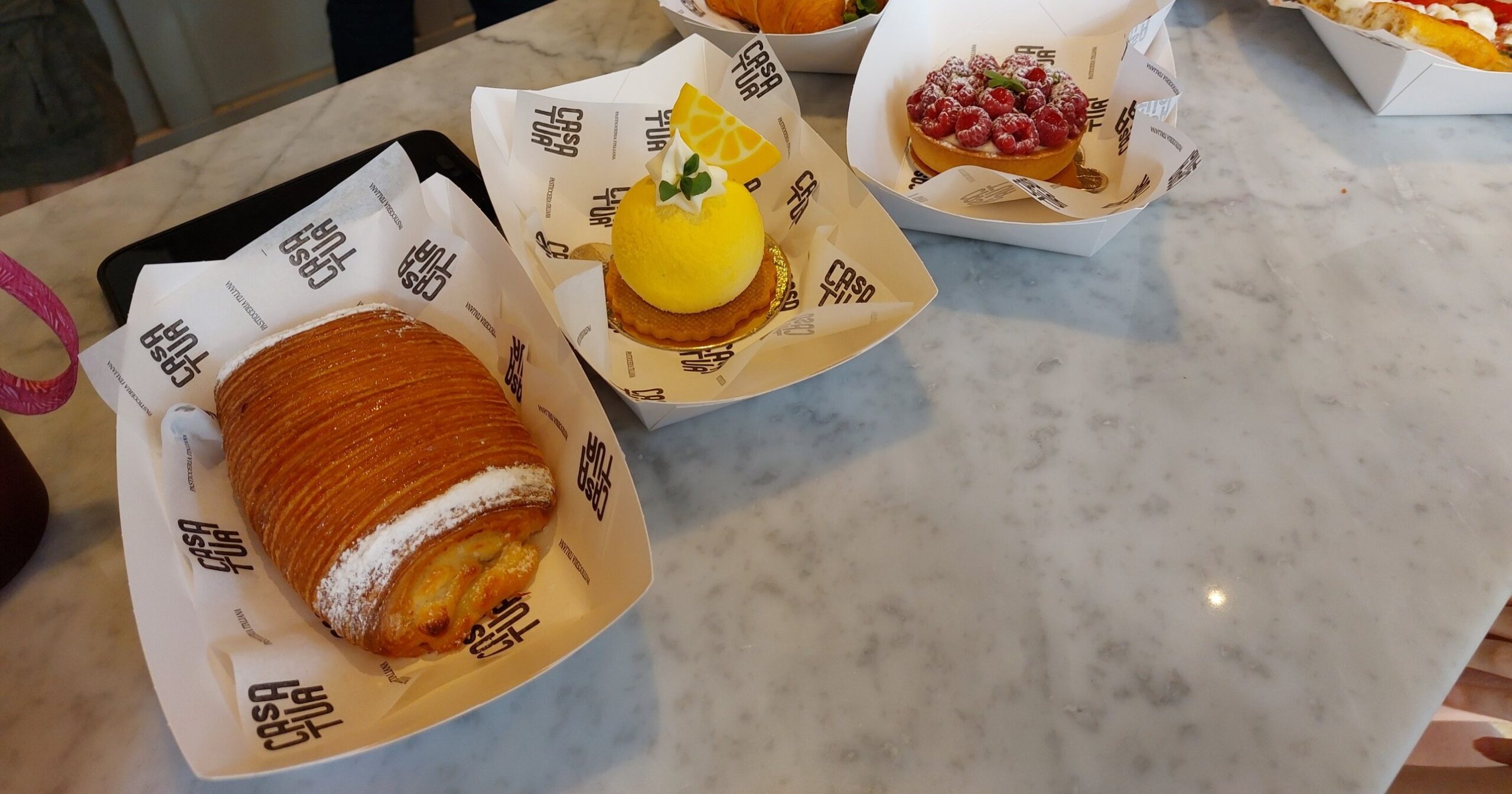A laminated involtino, a lemon dome dessert and a raspberry tart in Casa Tua paper boats on a marble counter