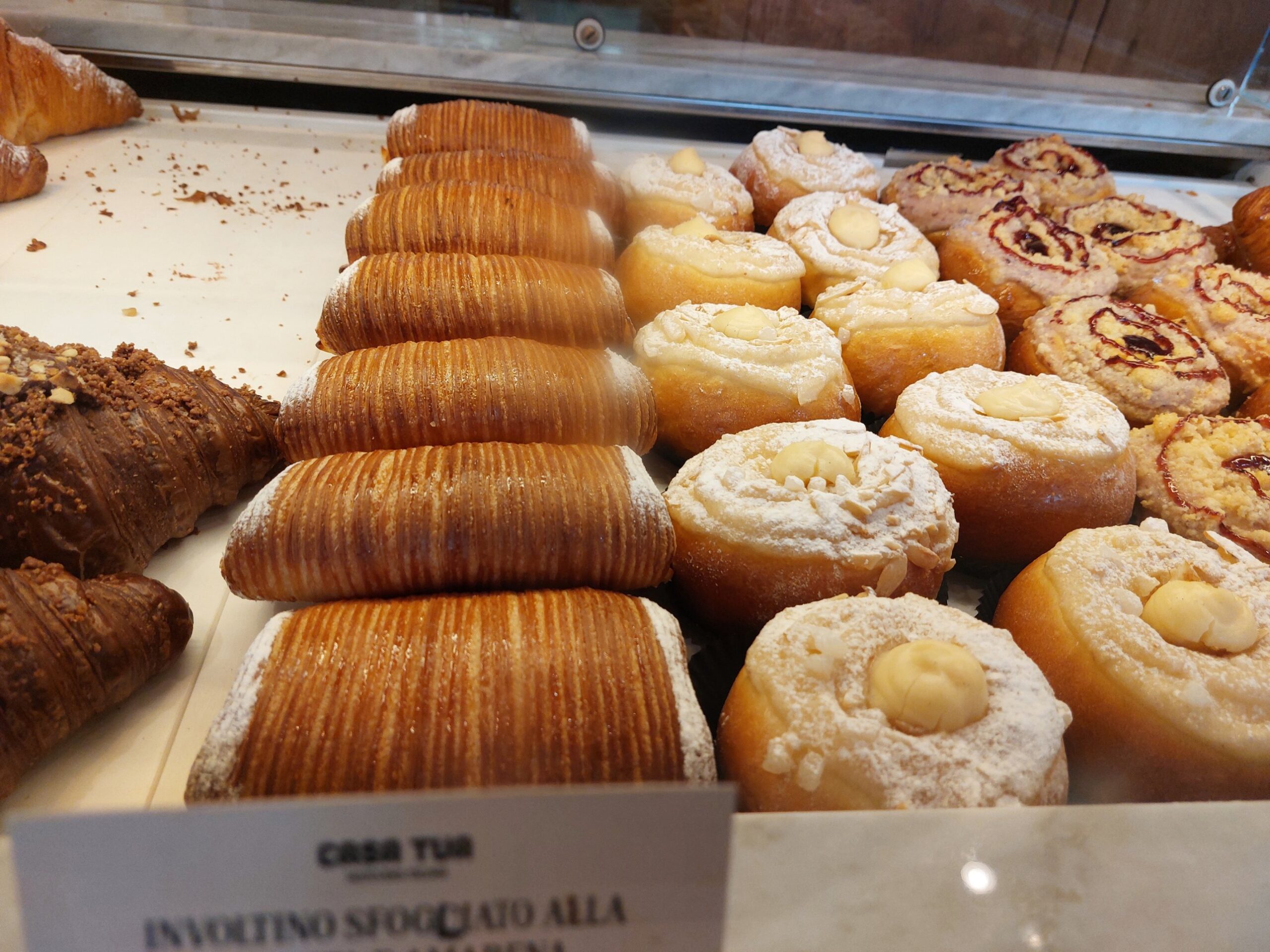Rows of ridged laminated involtino pastries next to sugar-dusted brioche with a dot of cream and berry ricotta brioche