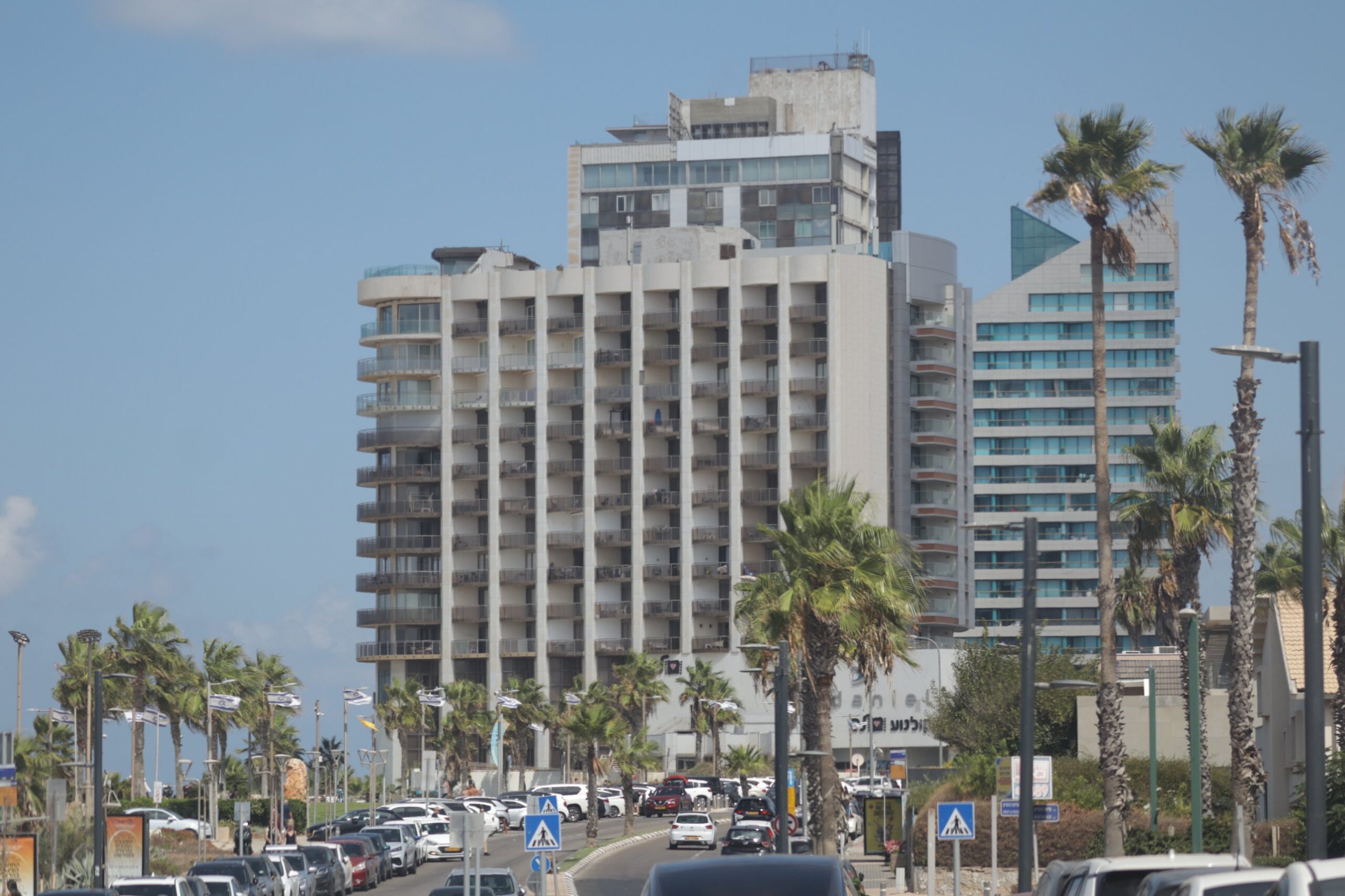 The Daniel Herzliya hotel tower above Ramot Yam Street, lined with palms and Israeli flags