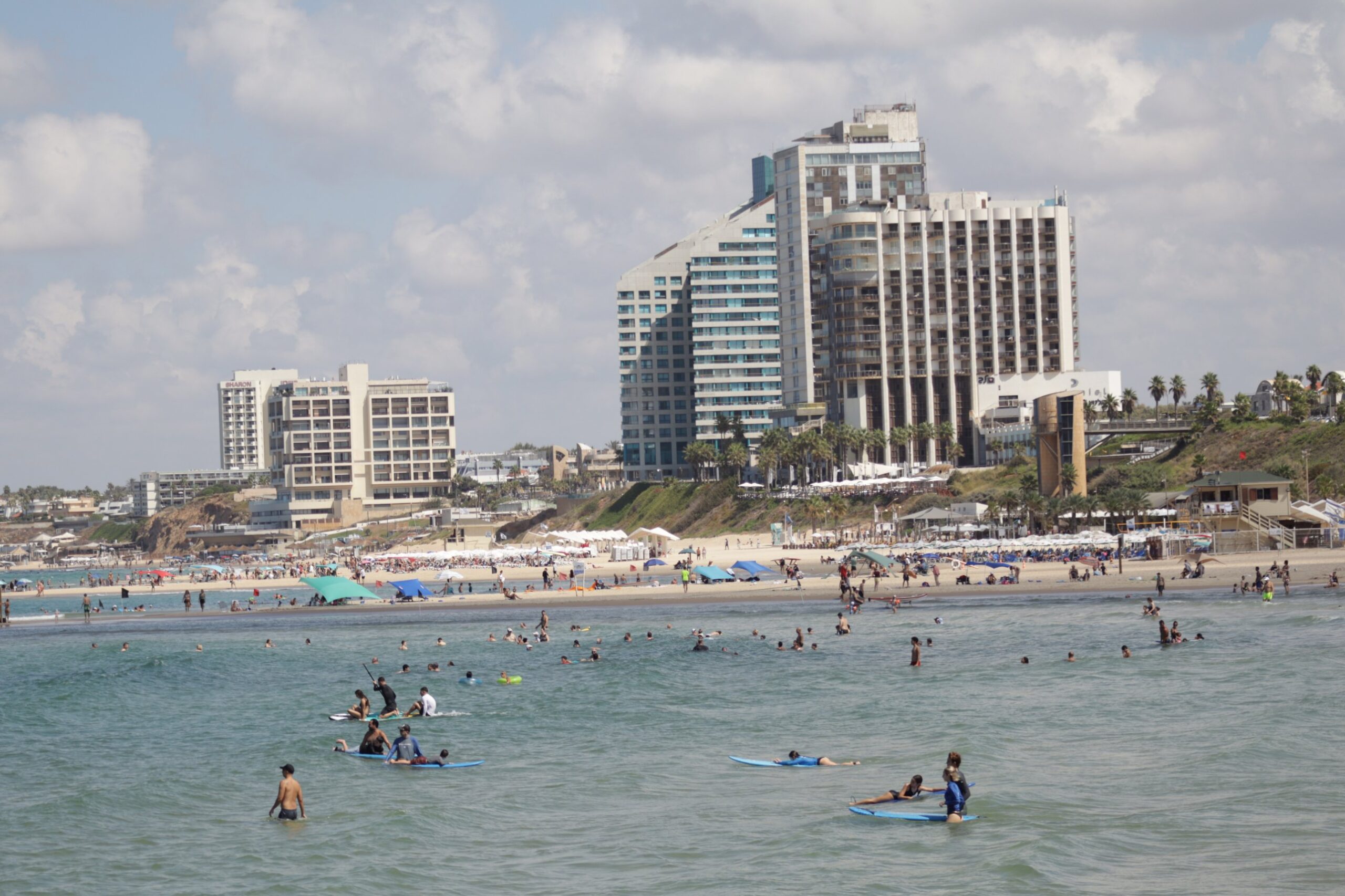 Surfers and swimmers off Herzliya beach, with the Sharon hotel and the Daniel Herzliya hotel on the cliff behind