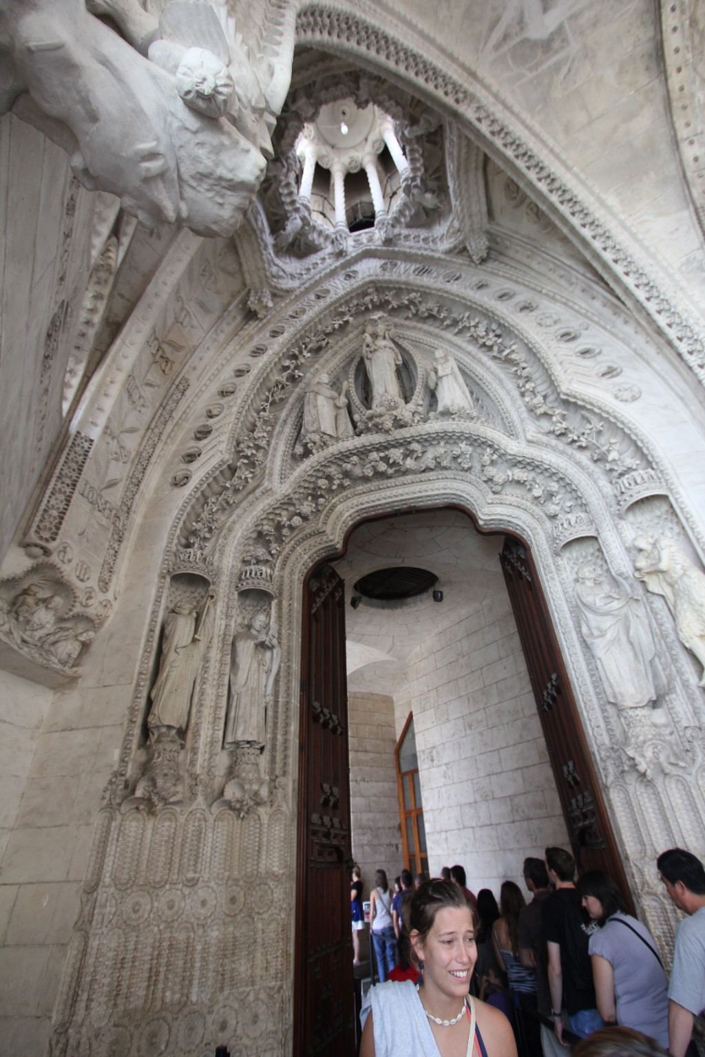 Visitors beneath sculpted figures and floral stone arches around a Sagrada Familia doorway in Barcelona